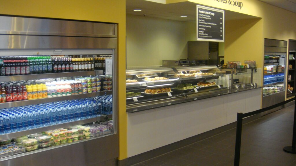 Modern cafeteria with food display counter and a chef at work in the kitchen area.