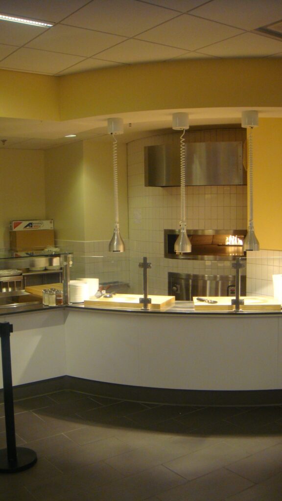 Modern cafeteria with food display counter and a chef at work in the kitchen area.