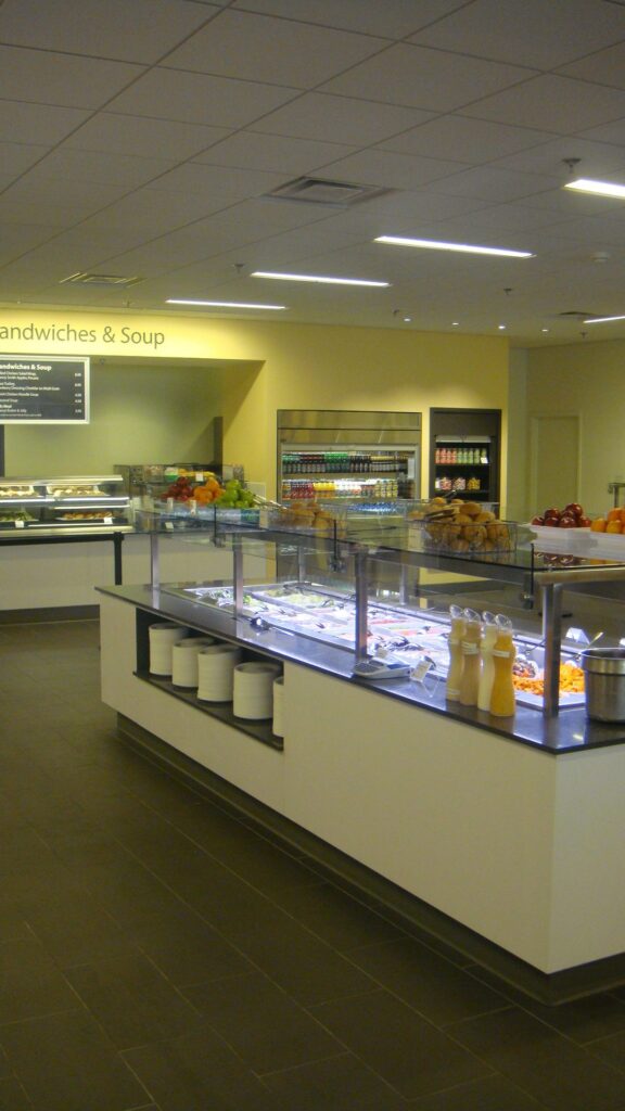 Modern cafeteria with food display counter and a chef at work in the kitchen area.