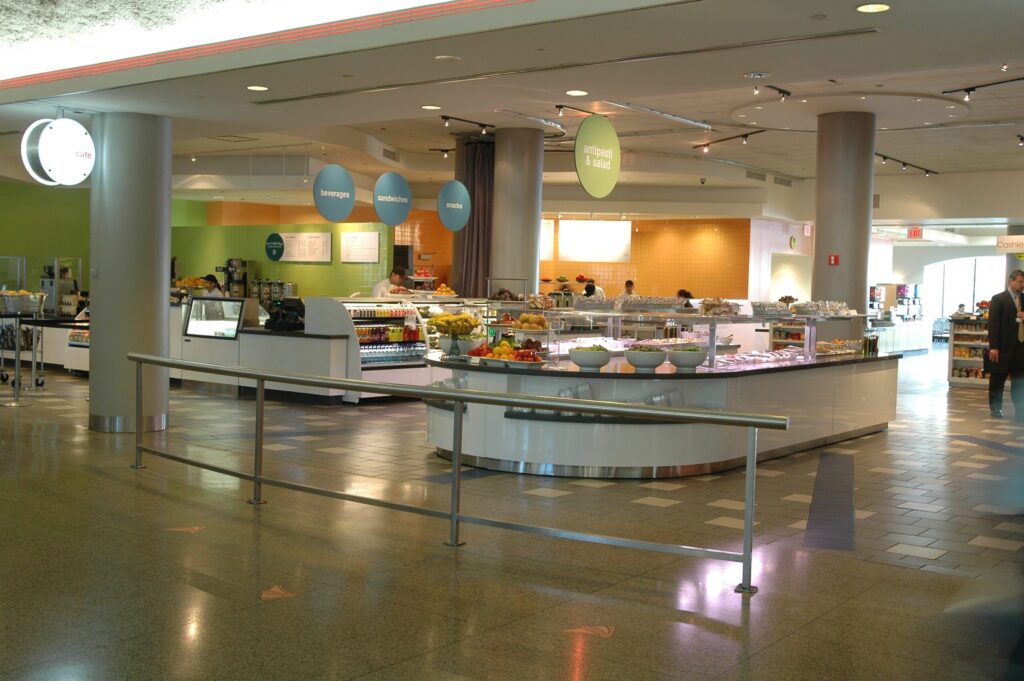 Modern cafeteria with food display counter and a chef at work in the kitchen area.