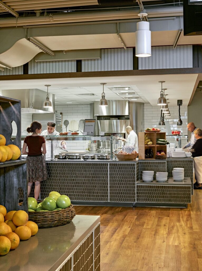 Modern cafeteria with food display counter and a chef at work in the kitchen area.