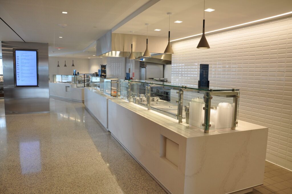 Modern cafeteria with food display counter and a chef at work in the kitchen area.