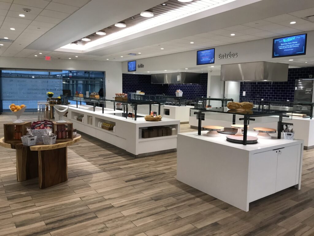 Modern cafeteria with food display counter and a chef at work in the kitchen area.