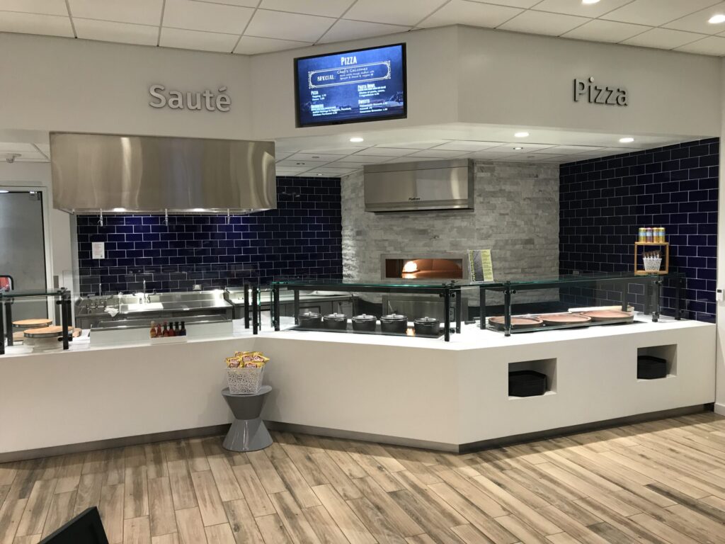 Modern cafeteria with food display counter and a chef at work in the kitchen area.