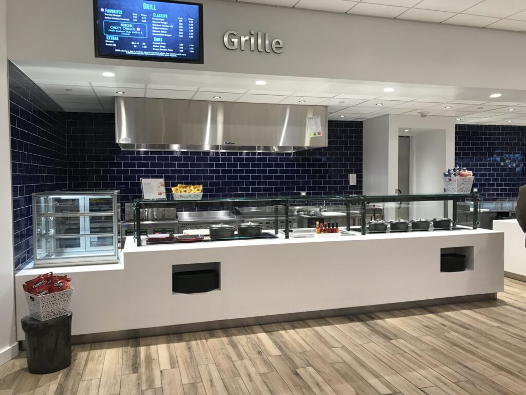 Modern cafeteria with food display counter and a chef at work in the kitchen area.