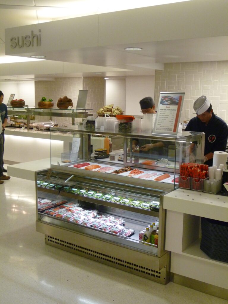 Modern cafeteria with food display counter and a chef at work in the kitchen area.