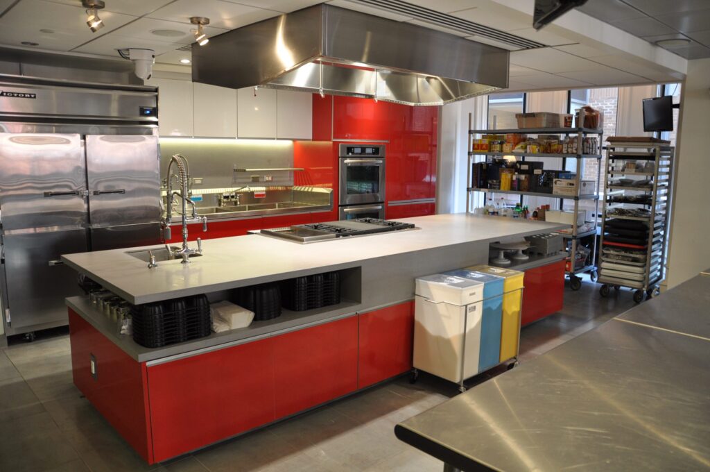 Modern cafeteria with food display counter and a chef at work in the kitchen area.