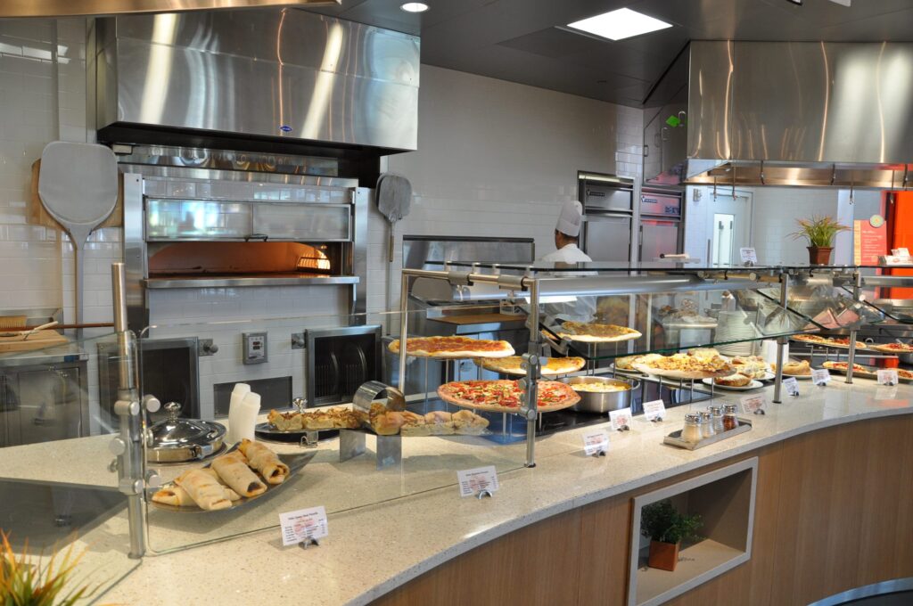 Modern cafeteria with food display counter and a chef at work in the kitchen area.