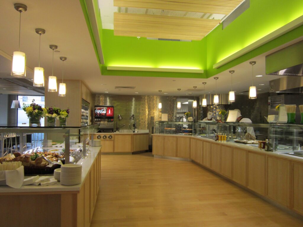 Modern cafeteria with food display counter and a chef at work in the kitchen area.