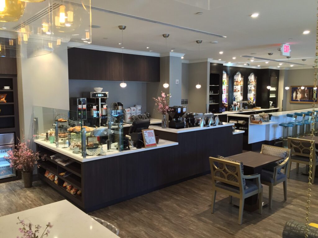 Modern cafeteria with food display counter and a chef at work in the kitchen area.