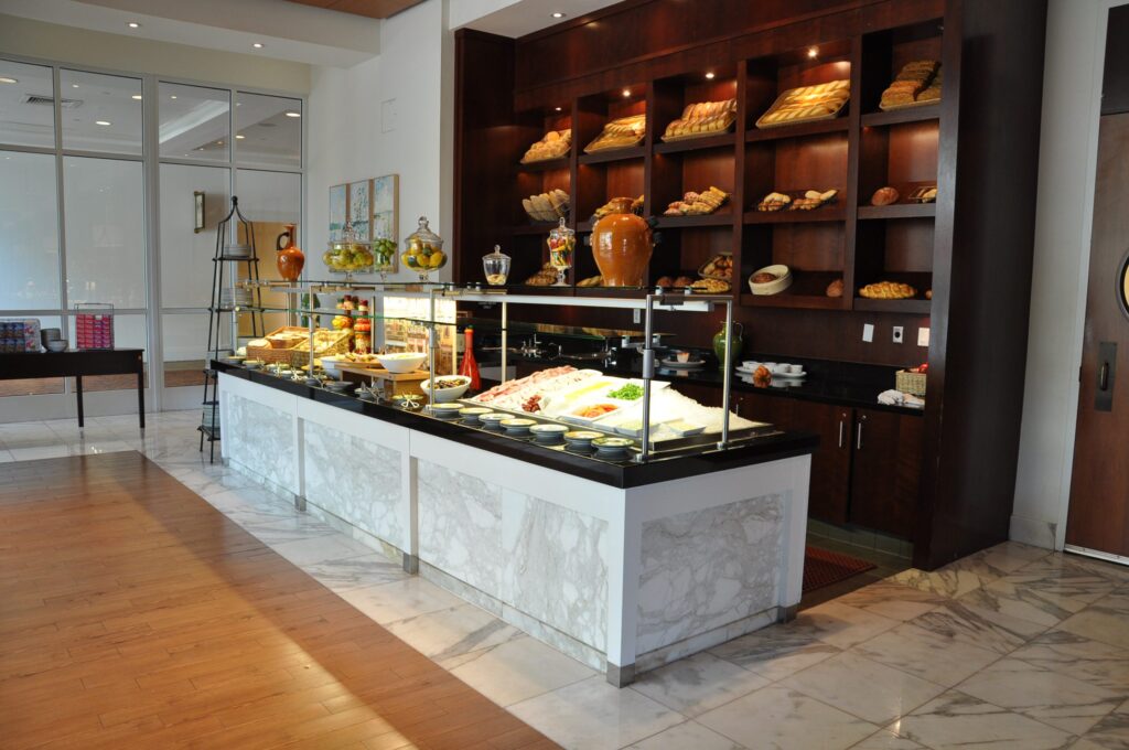 Modern cafeteria with food display counter and a chef at work in the kitchen area.