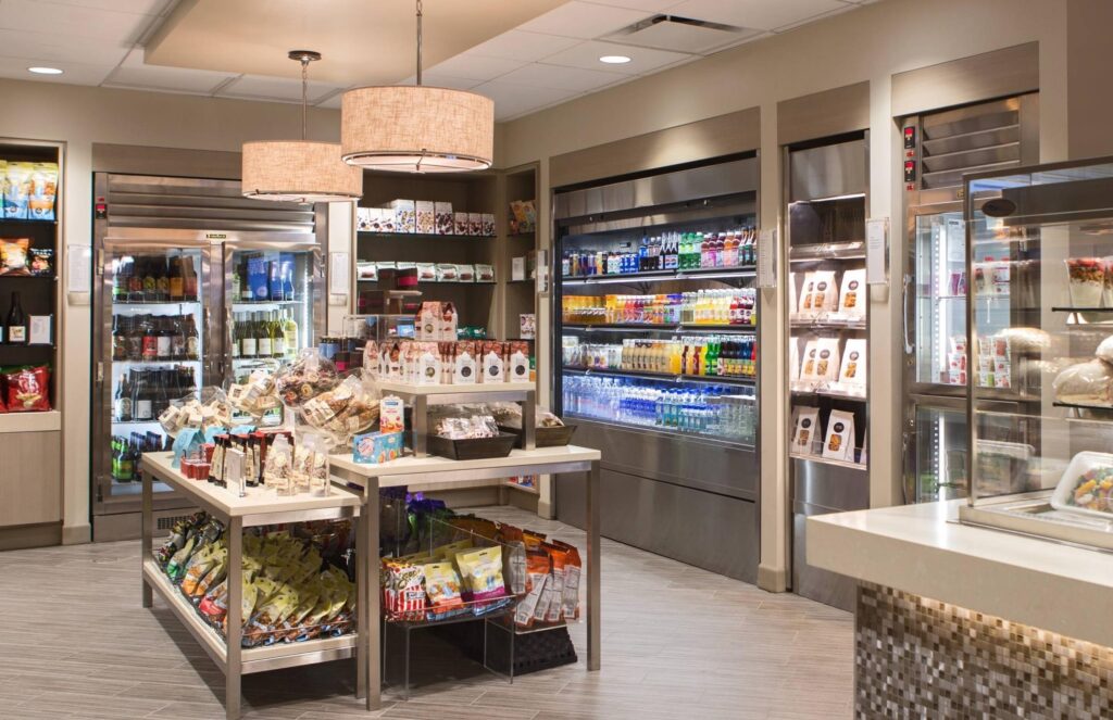 Modern cafeteria with food display counter and a chef at work in the kitchen area.