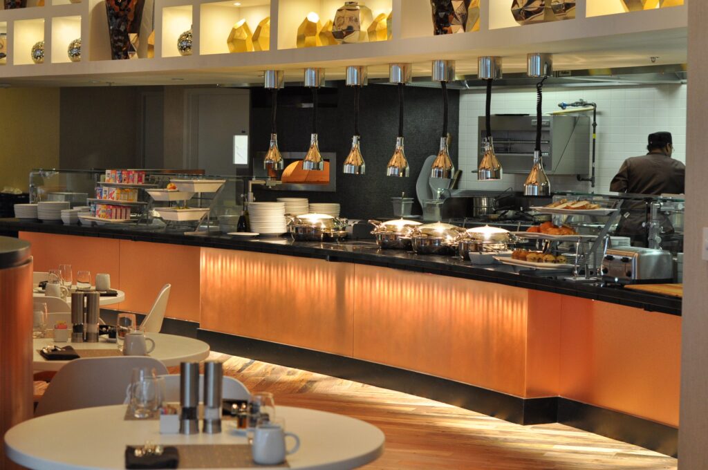 Modern cafeteria with food display counter and a chef at work in the kitchen area.