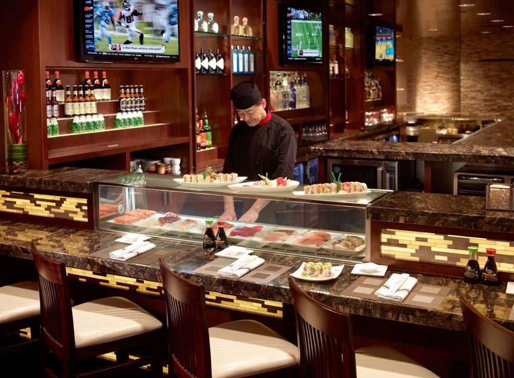 Modern cafeteria with food display counter and a chef at work in the kitchen area.