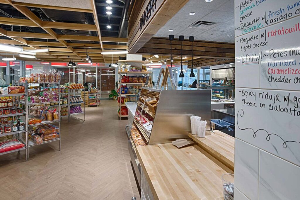 Modern cafeteria with food display counter and a chef at work in the kitchen area.