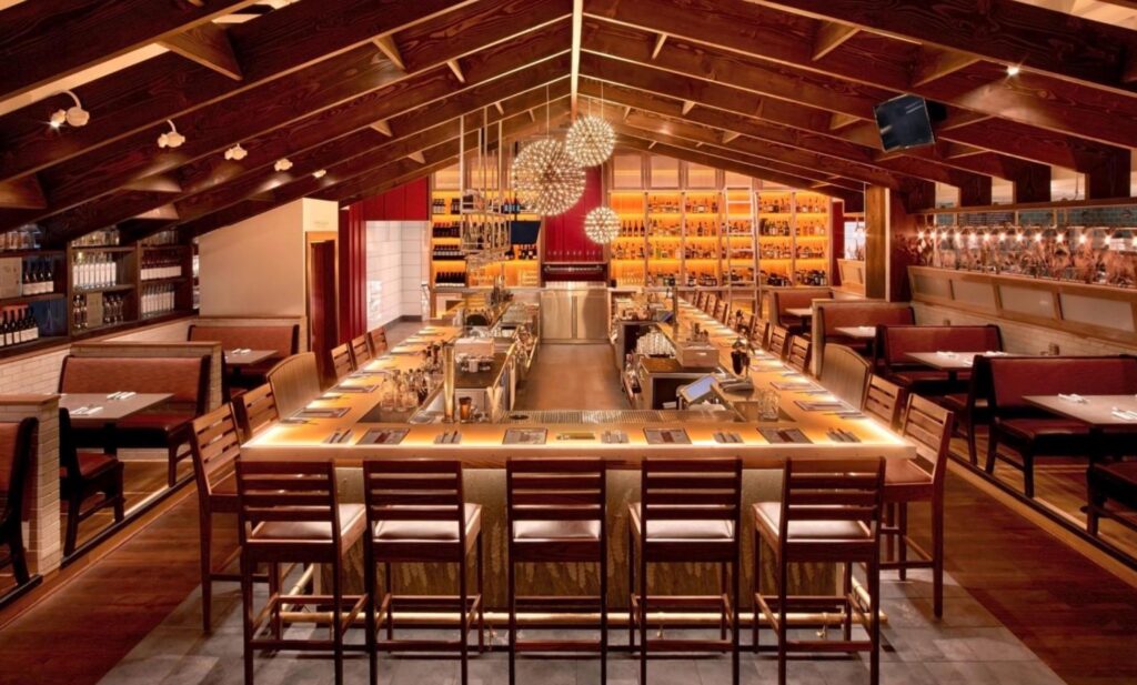 Modern cafeteria with food display counter and a chef at work in the kitchen area.