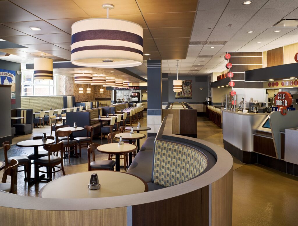 Modern cafeteria with food display counter and a chef at work in the kitchen area.